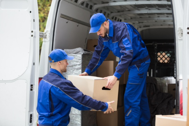 Two men in blue uniforms are loading boxes into a van, working together to organize the cargo efficiently.